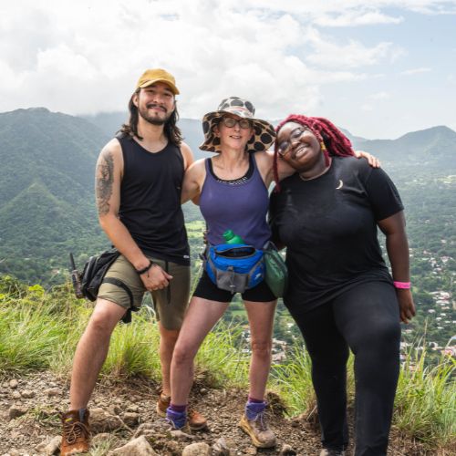 Three volunteers smiling at a mountain viewpoint with lush green hills behind them