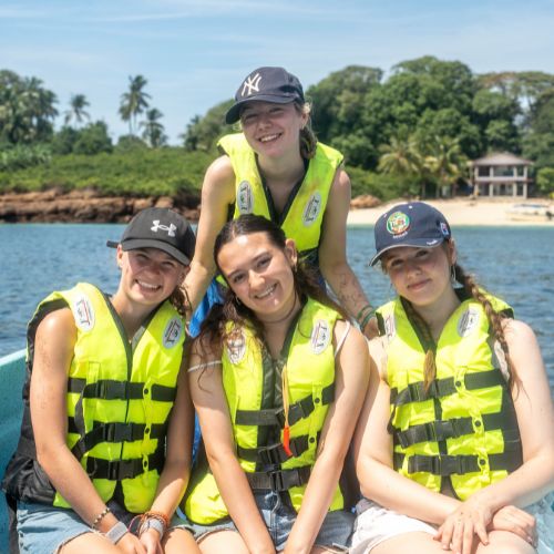Four volunteers wearing bright life vests sitting on a boat during a coastal excursion