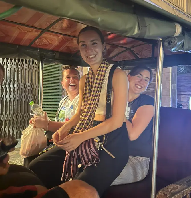 Smiling friends enjoy a tuk-tuk ride with vibrant decor, sharing laughter and camaraderie in an exciting urban setting.