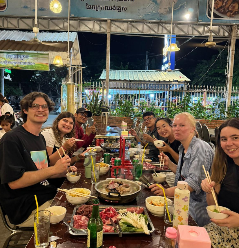 A lively group of friends enjoys a delicious outdoor barbecue dinner with fresh ingredients at a bustling night market.