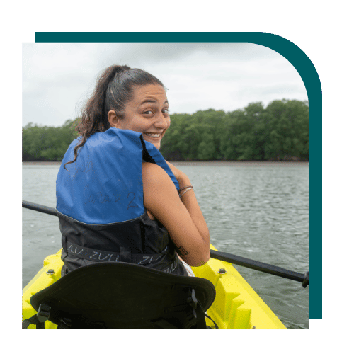 Smiling woman wearing a life jacket kayaking on a calm lake surrounded by trees