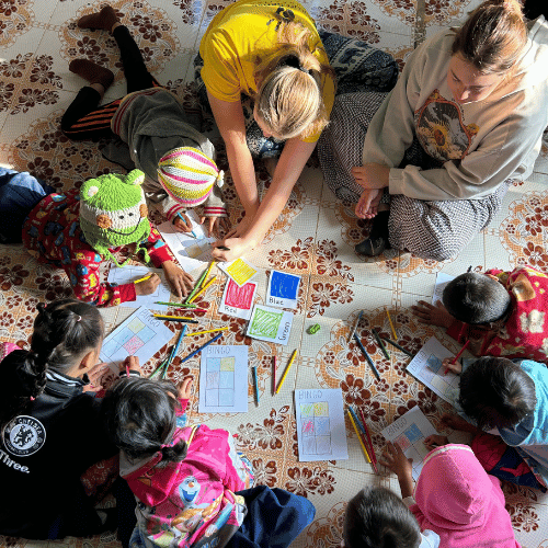 Volunteers sitting on the floor with children during a colouring activity as part of an education program