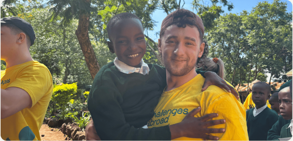 Volunteer in a yellow Challenges Abroad shirt holding and smiling with a young student outdoors