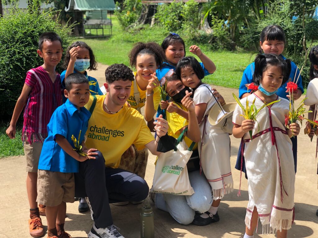 Volunteers in yellow Challenges Abroad shirts posing outdoors with smiling local children holding flowers