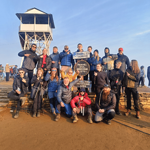 Group of Challenges Abroad volunteers posing at the Poon Hill viewpoint with signs and a lookout tower in the background