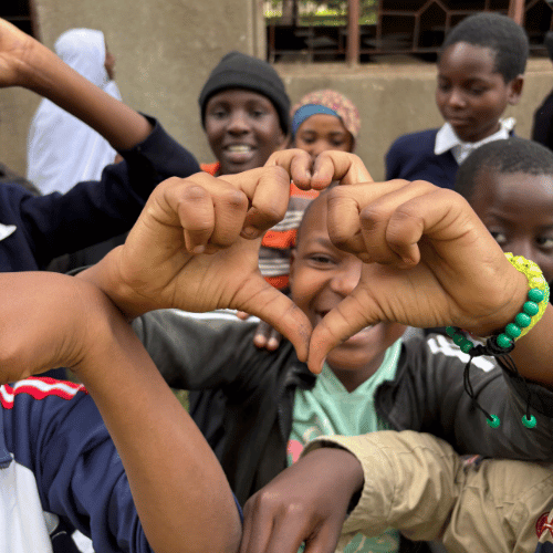 Smiling students forming a heart shape with their hands during a community program